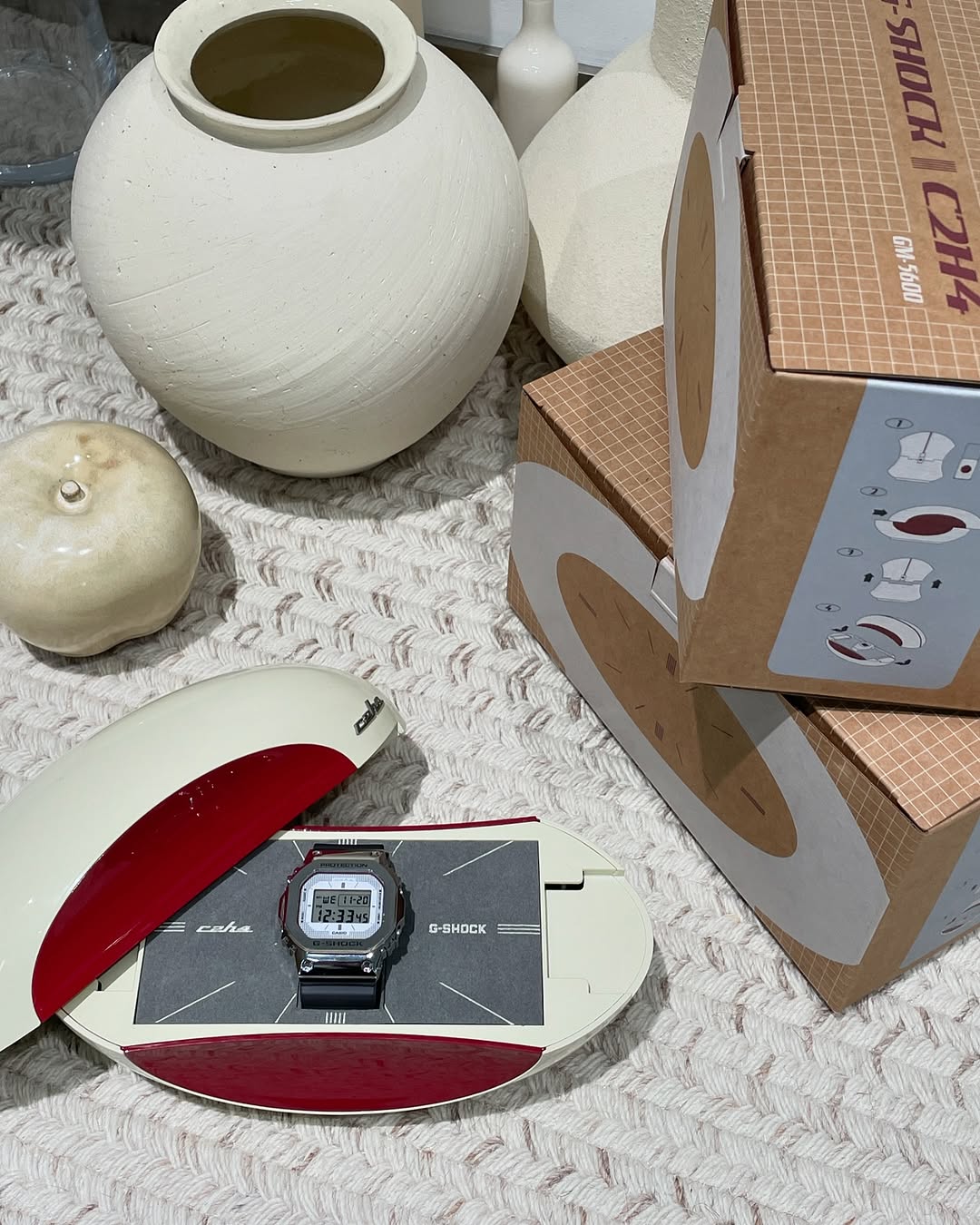 미래지향적인 C2H4 지샥🛸
2025년 1월, LA 기반 스트릿웨어 브랜드 C2H4와 G-SHOCK이 협업해 GM-5600 '스페이스 에이지'를 선보였습니다. 스테인리스 스틸 베젤과 반투명 회색 레진 스트랩에 레드 포인트를 더했으며, 다이얼은 그리드 패턴으로 사이버펑크적 감각을 강조했는데요.
1970년대 ATC Genie Telephone에서 영감을 받은 캡슐형 패키지는 오프 화이트와 레드 포인트, 하단 인쇄물이 특징입니다. 이미지4