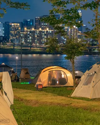 9월부터 한강 그늘막 밤 10시까지🌙
예약 5분 만에 마감됐다, 한강이 밤 10시까지 열린다⛺️🌊
9월부터 한강공원 그늘막을 밤 10시까지 칠 수 있습니다. 기존 오후 7시에서 3시간 늘었죠. 그늘막 허용구역도 16개소에서 20개소로 늘어, 광나루·잠실·뚝섬·양화한강공원에 한 곳씩 추가됩니다.
배달존은 3개 공원 6개소에서 11개 공원 17개소로 확대됩니다. 광나루·잠실·뚝섬·잠원·반포·이촌·여의도·양화·망원·난지·강서한강공원이 대상이죠. 야간 이용이 느는 만큼 조명등과 CCTV를 추가하고 순찰과 쓰레기 수거도 강화합니다.
8월 여의도·뚝섬에서 열린 '한강 밤핑'이 계기가 됐습니다. 한 달간 3,503팀 1만 1,476명이 참여했고, 금·토요일 회차는 예약 시작 5분 만에 마감됐죠. 이용객 94.7%가 내년에도 운영되길 바란다고 답했습니다. 이미지