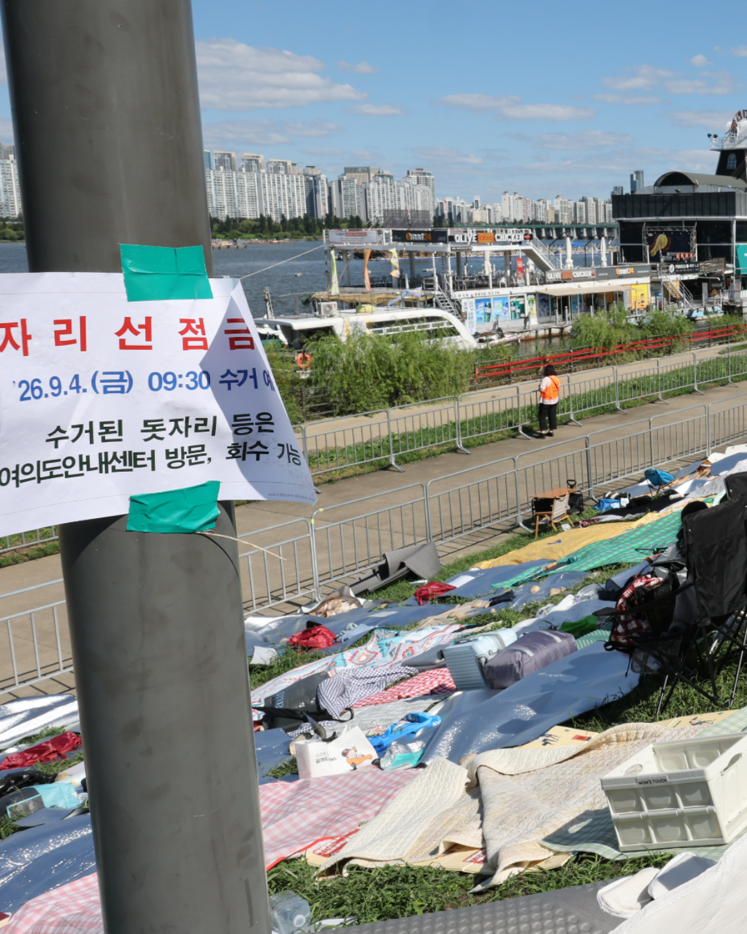 여의도에 빈 돗자리가 깔렸습니다 🧺
서울시가 오늘 오전 9시 30분을 못 박았습니다
서울시가 9월 4일 오전 9시 30분을 기해 여의도한강공원의 주인 없는 돗자리를 걷어내겠다고 못 박았습니다. 서울세계불꽃축제는 4일 전야제, 5일 본행사로 열립니다. 불꽃쇼는 5일 저녁 8시부터 9시 10분까지죠.
중고거래 앱에는 명당을 넘기겠다는 글이 줄줄이 올라왔습니다. 4인 자리 25만원, 돗자리 서너 장은 60만원이죠. 강이 보이는 식당 2인석은 600만원까지 붙었습니다. 빈 돗자리에는 쪽지가 놓였습니다. "잠시 자리 비웠습니다. 근처에 있어요. 건드리지 말아주세요."
한강공원은 누구나 쓰는 공공장소입니다. 서울시 관계자는 "공원에서 누군가 밤새 앉아 있다고 규제할 수 없는 것처럼" 돗자리를 막을 근거가 없다고 설명했습니다. 계고장을 붙이고 주인 없는 것만 회수하는 게 전부죠. 대형 행사 하루 전 자리 선점을 금지하는 조례 개정이 거론되지만 아직 논의 전입니다. 이미지1
