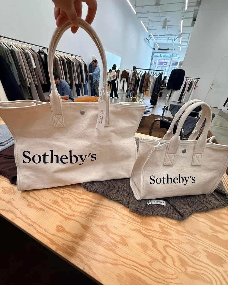 281년 소더비와 만든 협업💛🖤실물
예술을 사고 드는 기분🖼️ 프레임 x 소더비 한정 컬렉션
켄달 제너가 요즘 자주 입고 모델인 프레임(FRAME)의 경매사 소더비 협업 실물이에요. 281년 된 경매장 로고를 데님 브랜드가 그대로 가져다 쓴 컬렉션입니다. 뉴욕 매장에서 직접 봤어요.
인기 제품 중 하나는 캔버스 토트백입니다. 크림 코튼 바탕에 블랙 세리프 로고만 크게 얹었고, 로프 손잡이와 스냅 하나가 전부예요. 라지와 스몰 두 사이즈로 나오는데 각각 200달러대와 160달러대죠.
캡은 페일 옐로우·레드·투톤 네이비 세 가지고, 니트는 가슴에 작은 레드 자수를 넣었습니다. 다크 네이비 스웨이드 집업도 함께 걸려 있었어요. 소더비가 옷을 낸 건 프레임이 처음입니다.
• 소더비 라지 토트백
• 소더비 스몰 토트백
• 소더비 베이스볼 캡
• 소더비 니트
• 소더비 스웨이드 자켓 이미지2