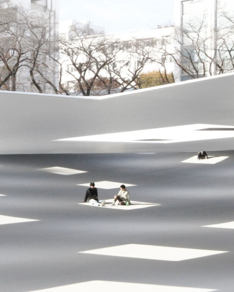 도쿄 여행 저장 필수 KAIT PLAZA🏛️
알고 보면 보테가 베네타 선정, 건축가의 영감 넘치는 작품🩷✨
기둥이 하나도 없습니다. 일본 가나가와현 아쓰기시 가나가와 공과대학의 ‘KAIT 플라자'는 4,100㎡ 규모의 실내 광장입니다. 바닥은 최대 5m 높이 차로 완만하게 기울고, 천장은 2.2~2.8m로 낮게 깔렸는데요. 지평선 아래 동굴에 들어온 듯한 느낌은 여기서 나옵니다.
천장에 뚫린 사각 창 59개로 햇살이 쏟아집니다. 비 오는 날에는 빗방울이 그대로 실내로 떨어지고, 물이 스며드는 바닥이 빗물을 곧바로 흡수합니다.
설계는 건축가 이시가미 준야(Junya Ishigami, 52)가 맡았습니다. 그는 이달 보테가 베네타와 함께 제정된 '바라간상(The Barragán Prize)'의 첫 수상자로 선정됐죠. 라이즈 원빈의 트레일러 배경으로도 알려진 곳이에요. 이미지1