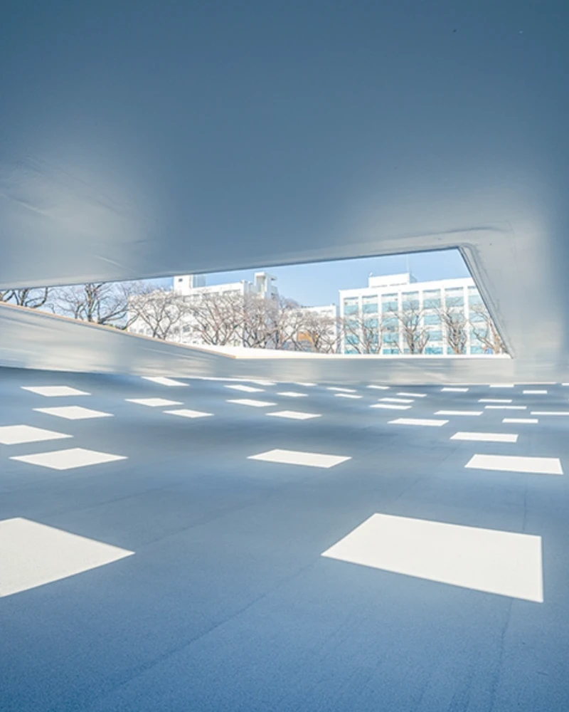 도쿄 여행 저장 필수 KAIT PLAZA🏛️
알고 보면 보테가 베네타 선정, 건축가의 영감 넘치는 작품🩷✨
기둥이 하나도 없습니다. 일본 가나가와현 아쓰기시 가나가와 공과대학의 ‘KAIT 플라자'는 4,100㎡ 규모의 실내 광장입니다. 바닥은 최대 5m 높이 차로 완만하게 기울고, 천장은 2.2~2.8m로 낮게 깔렸는데요. 지평선 아래 동굴에 들어온 듯한 느낌은 여기서 나옵니다.
천장에 뚫린 사각 창 59개로 햇살이 쏟아집니다. 비 오는 날에는 빗방울이 그대로 실내로 떨어지고, 물이 스며드는 바닥이 빗물을 곧바로 흡수합니다.
설계는 건축가 이시가미 준야(Junya Ishigami, 52)가 맡았습니다. 그는 이달 보테가 베네타와 함께 제정된 '바라간상(The Barragán Prize)'의 첫 수상자로 선정됐죠. 라이즈 원빈의 트레일러 배경으로도 알려진 곳이에요. 이미지2