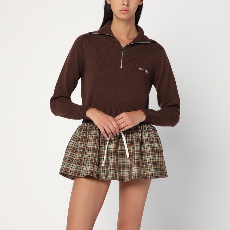 코코아 색상의 미우미우 캐시미어 스웨터는 앞면 지퍼가 달린 높은 숄 칼라, 긴 소매, 리브 커프스와 밑단, 가슴 부분에 로고 자수가 특징입니다. 이미지