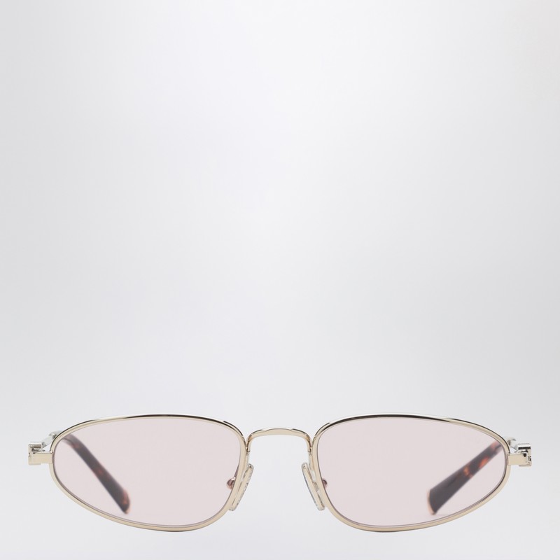 골드 메탈 소재의 미우미우 선글라스는 밝은 핑크색 타원형 렌즈와 세로 로고가 새겨진 얇은 안경다리가 특징입니다. 처방 렌즈와 호환되는 프레임입니다. 이미지