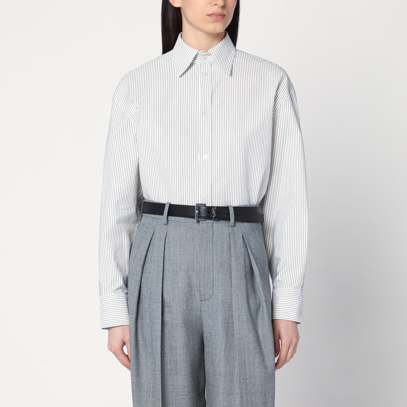 검은색 줄무늬가 있는 흰색 코튼 생 로랑 셔츠, 뾰족한 칼라, 단추로 고정된 커프스가 있는 긴 소매, 곡선 밑단, 앞 단추, 그리고 대조되는 작은 자수 Cassandre 로고가 특징입니다. 이미지