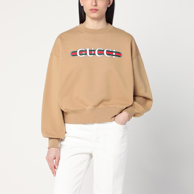 카라멜 코튼 소재의 구찌 크루넥 스웨트셔츠는 긴 소매, 리브 가장자리, 가슴 부분에 대조적인 녹색/빨간색/녹색 웹 리본이 달린 로고 문자 프린트가 특징입니다. 이미지
