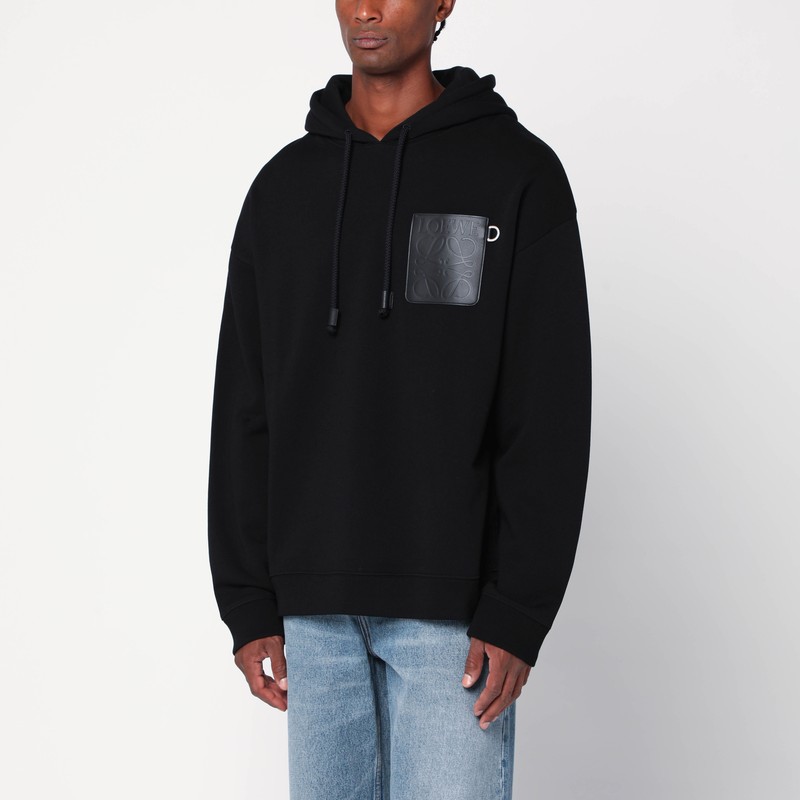 검은색 코튼 로에베 스웨트셔츠는 끈이 달린 후드, 긴 소매, 리브 가장자리, 가슴에 아나그램 로고와 D링이 새겨진 가죽 포켓, 여유로운 핏이 특징입니다. 이미지