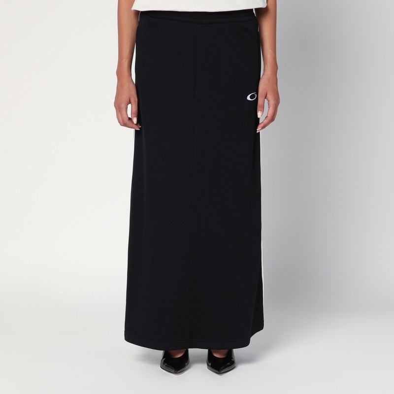 허리에 끈이 달린 디자인, 옆주머니 두 개, 옆면에 대조적인 흰색 밴드, 앞면에 로고가 들어간 검은색 코튼 발렌시아가 롱 스커트입니다. 이미지