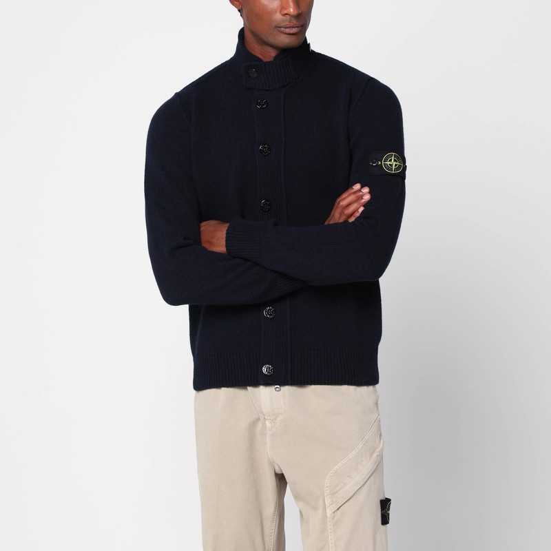 스톤 아일랜드의 네이비 블루 울 블렌드 가디건은 앞 단추 잠금 장치, 긴 소매(소매 중 하나에 컴퍼스 로고 라벨 있음), 단추로 잠그는 플래킷이 있는 높은 칼라, 리브 가장자리가 특징입니다. 이미지