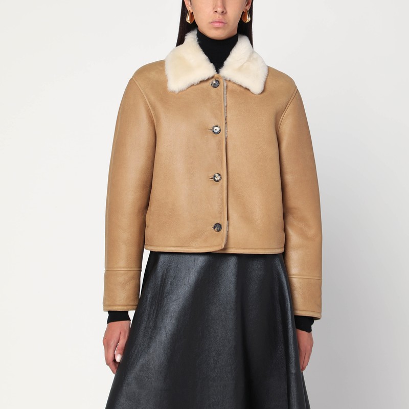 부드러운 베이지색 캐멀 메리노 셰어링 소재의 로에베 숏 코트는 넓은 칼라, 긴 소매, 앞면 버튼 잠금 장치, 웰트 포켓 2개, 뒷면에 아나그램 로고가 있는 가죽 패치가 특징입니다. 이미지