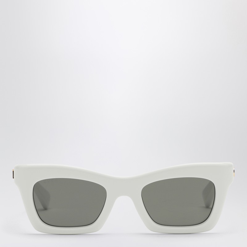 구찌의 흰색 광택 아세테이트 선글라스는 직사각형 모양, 관자놀이 부분에 양각된 골드톤 메탈 로고, 단색 회색 렌즈가 특징입니다. 이미지