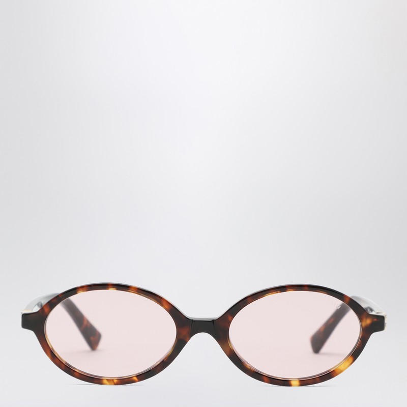 타원형 프레임, 100% UVA/UVB 보호 기능이 있는 핑크 렌즈, 로고가 새겨진 템플이 특징인 Honey Havana 아세테이트 소재의 Miu Miu 선글라스입니다. 처방 안경과 호환되지 않는 프레임입니다. 이미지