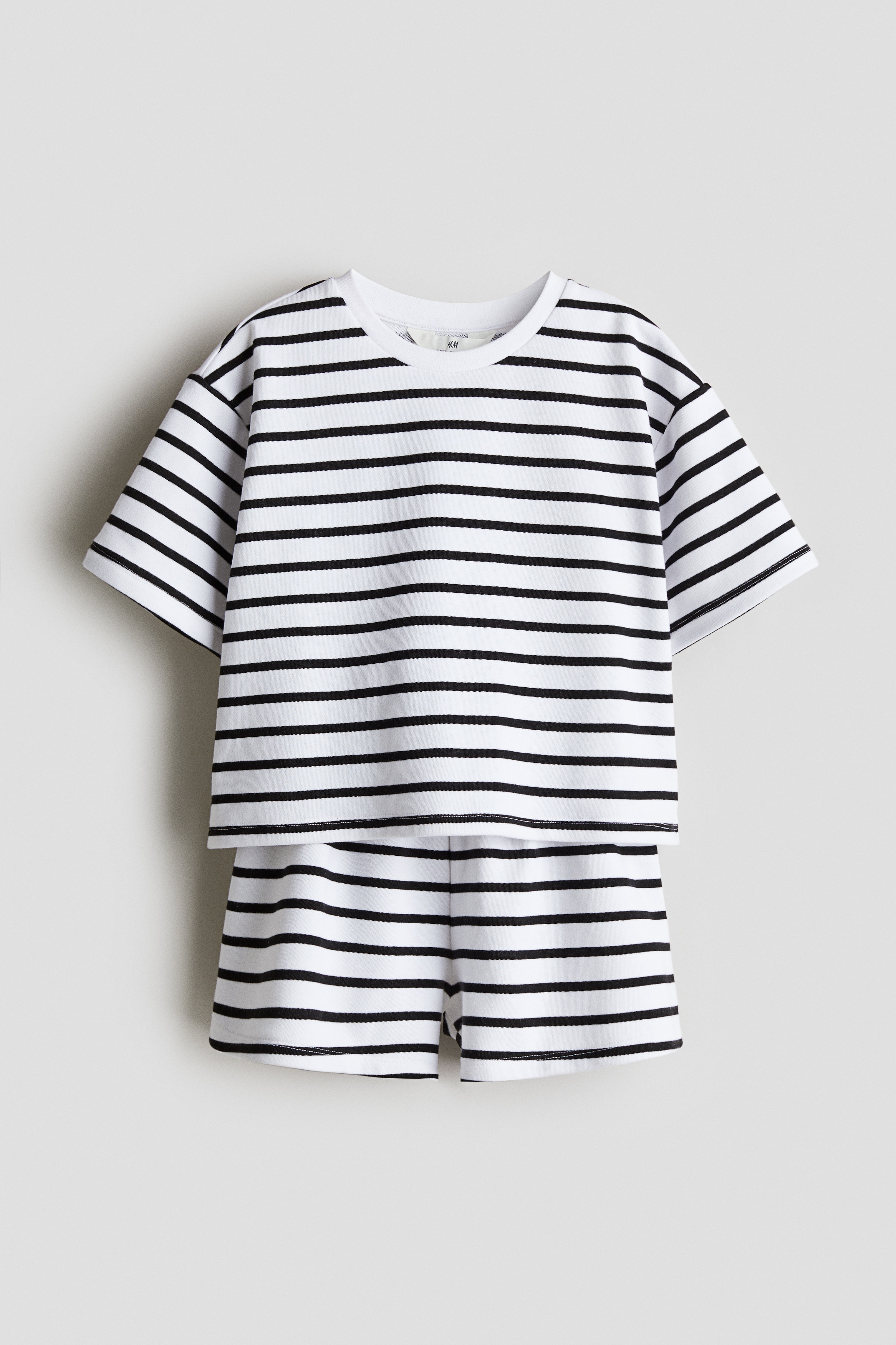 가벼운 스웨트셔츠 소재의 포근한 상하의 세트. 상의 - 드롭 숄더 스타일의 티셔츠. 리브드 라운드넥. 옆면에 짧은 트임이 있는 스트레이트 헴라인. 하의 - 허릿단에 밴딩이 내장된 반바지. 이미지