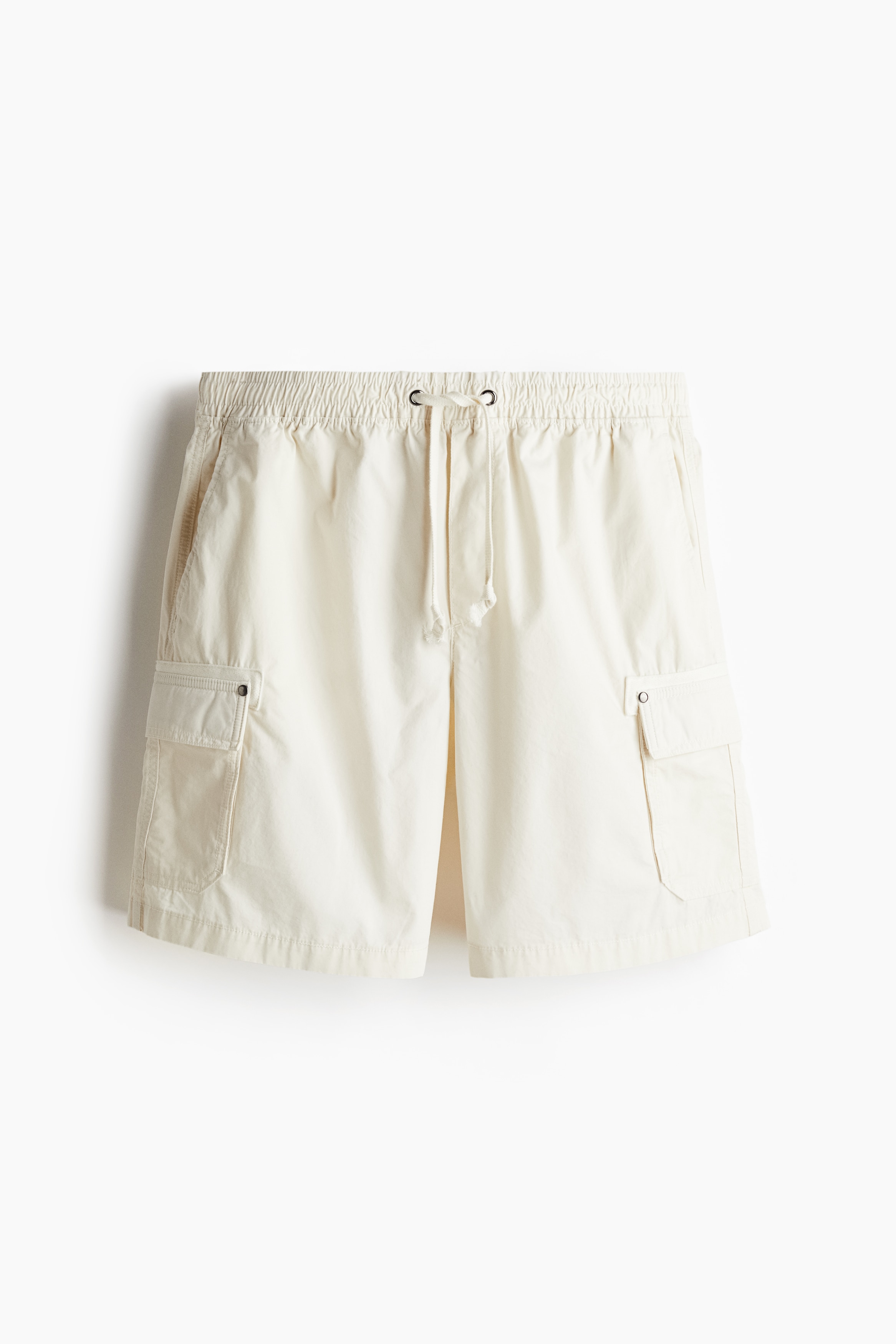 코튼 포플린 소재의 카고 반바지. 드로스트링이 있는 신축성 허릿단. 페이크 플라이. 사선 방향의 옆면 포켓, 뒷면 포켓, 스냅버튼이 있는 다리 플랩포켓. 옆면 하단에 짧은 트임이 있는 아랫단. 캐주얼하지만 오버사이즈보다 피트되는 릴랙스핏 실루엣. 이미지