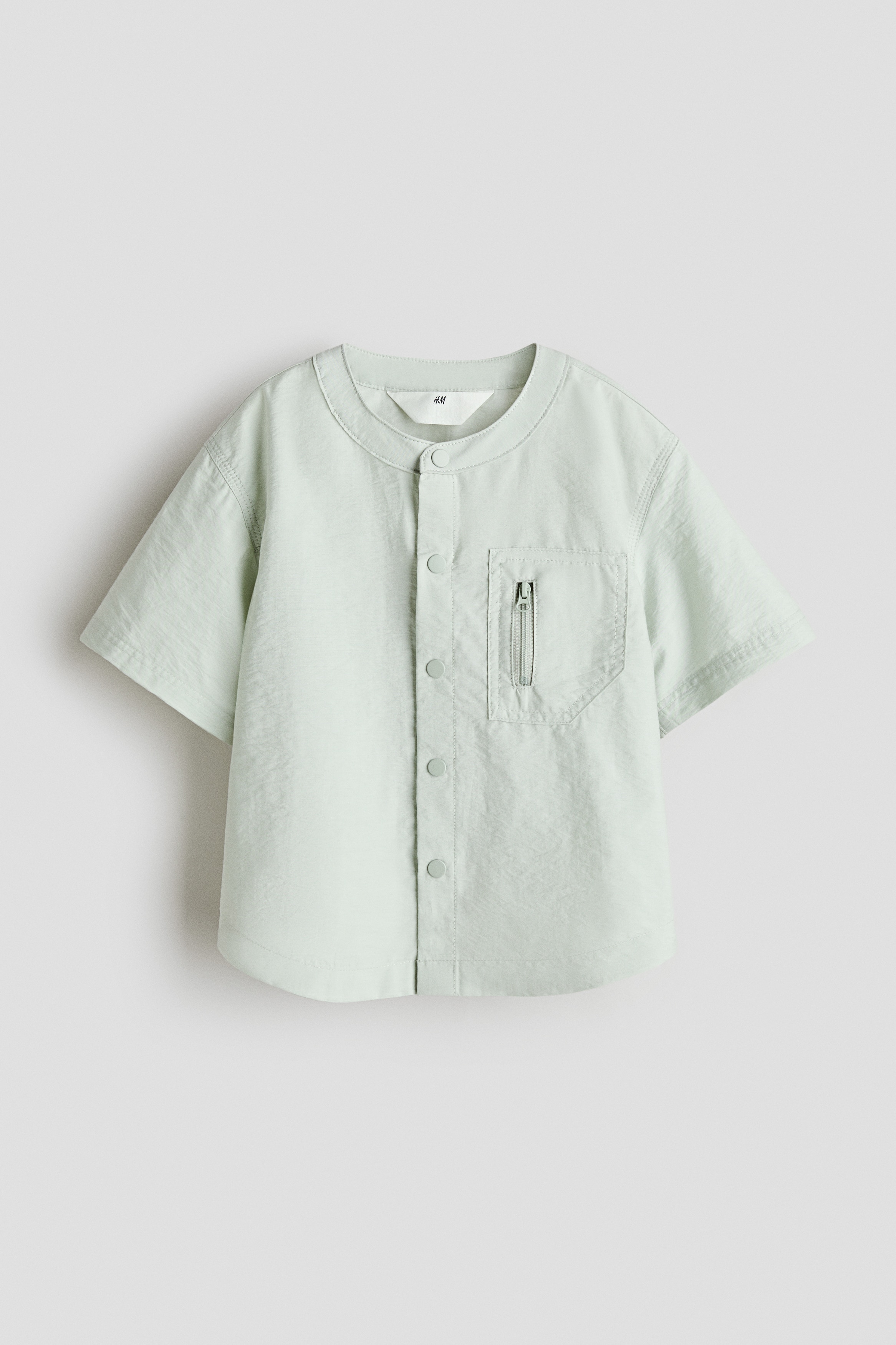 부드러운 코튼, 나일론 혼방 소재의 오버사이즈 오버셔츠. 라운드넥. 앞면 스냅버튼 클로저. 가슴 지퍼 포켓. 세미 드롭 숄더. 반소매. 라운드 헴라인. 이미지