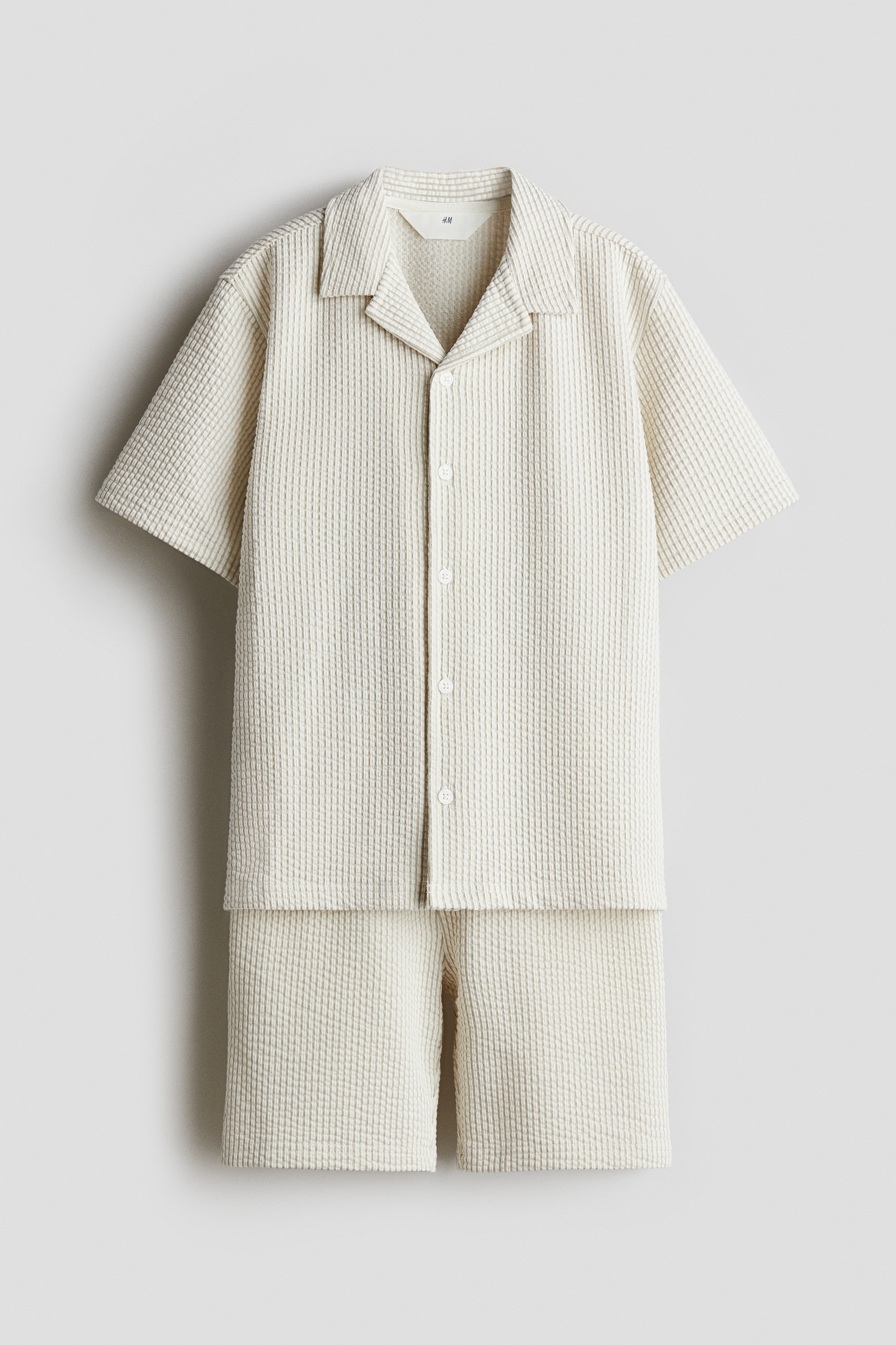 시어서커 느낌을 주는 부드러운 저지 소재의 상하의 세트. 상의 - 버튼업 스타일의 반소매 셔츠. 캠프 칼라. 드롭 숄더. 하의 - 드로스트링이 있는 신축성 허릿단의 반바지. 옆면 히든 포켓. 이미지