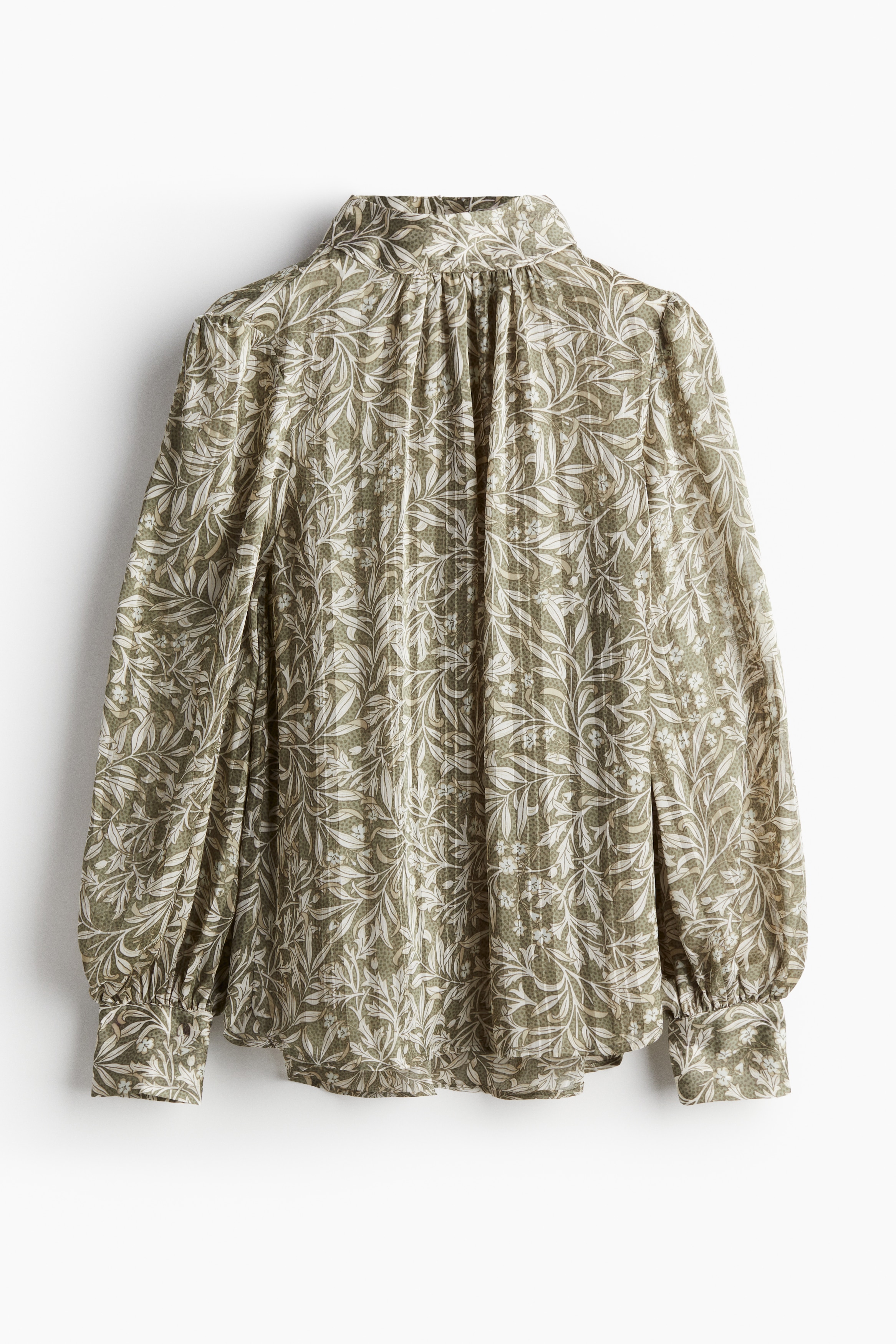 패턴이 있는 투명한 크레이프 소재의 블라우스. 짧은 스탠드 칼라. 목 뒷면에 키홀 트임과 커버드 버튼이 있음. 어깨 부분이 주름을 잡은 긴소매. 커버드 버튼이 있는 소맷단. 세미 라운드 헴라인. 이미지