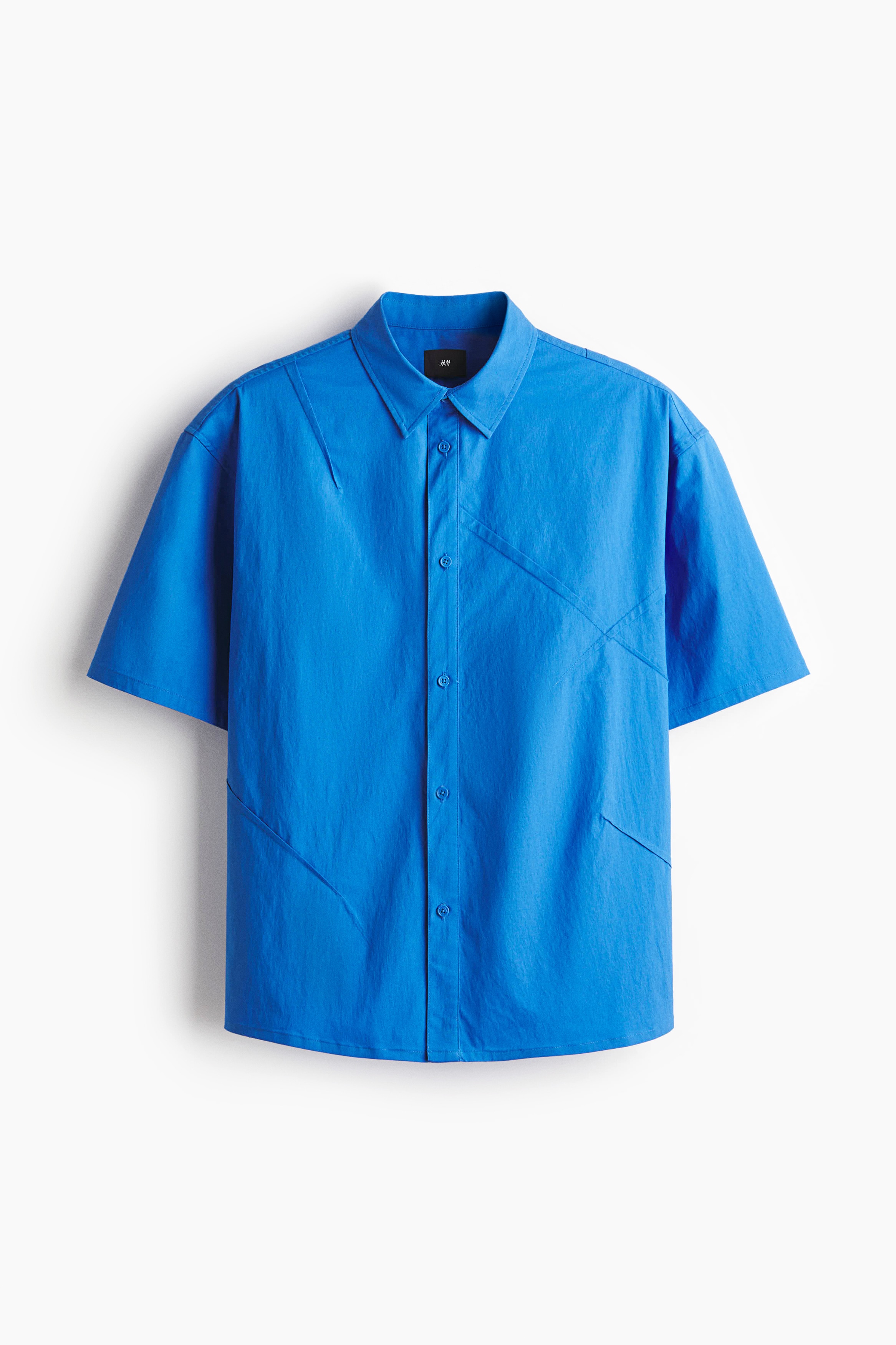 부드러운 코튼, 나일론 혼방 소재의 반소매 셔츠. 다트를 박음질처리하여 크리스 패턴을 연출한 디자인. 턴다운 칼라. 버튼단이 있는 클래식 프런트 스타일. 뒷면 요크. 세미 라운드 헴라인. 넉넉하지만 오버사이즈보다는 약간 피트되는 루즈핏 실루엣. 이미지