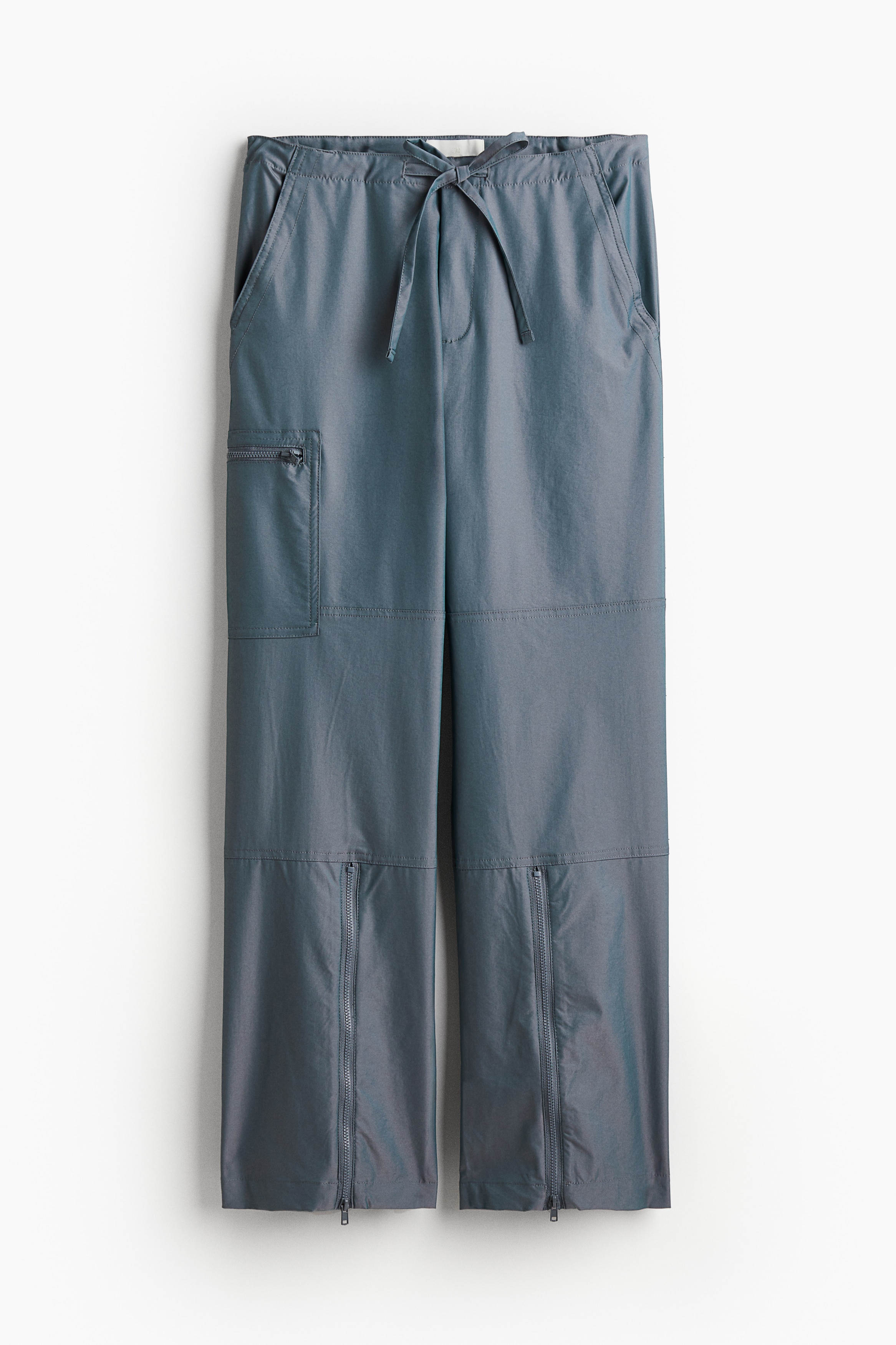 허릿단에 드로스트링이 있는 트윌 팬츠. 사선 방향의 옆면 포켓. 테이프로 여닫는 뒷면 플랩포켓. 지퍼로 여닫는 다리 포켓. 수퍼 롱 레그. 아랫단 앞면에 지퍼가 있음. 이미지