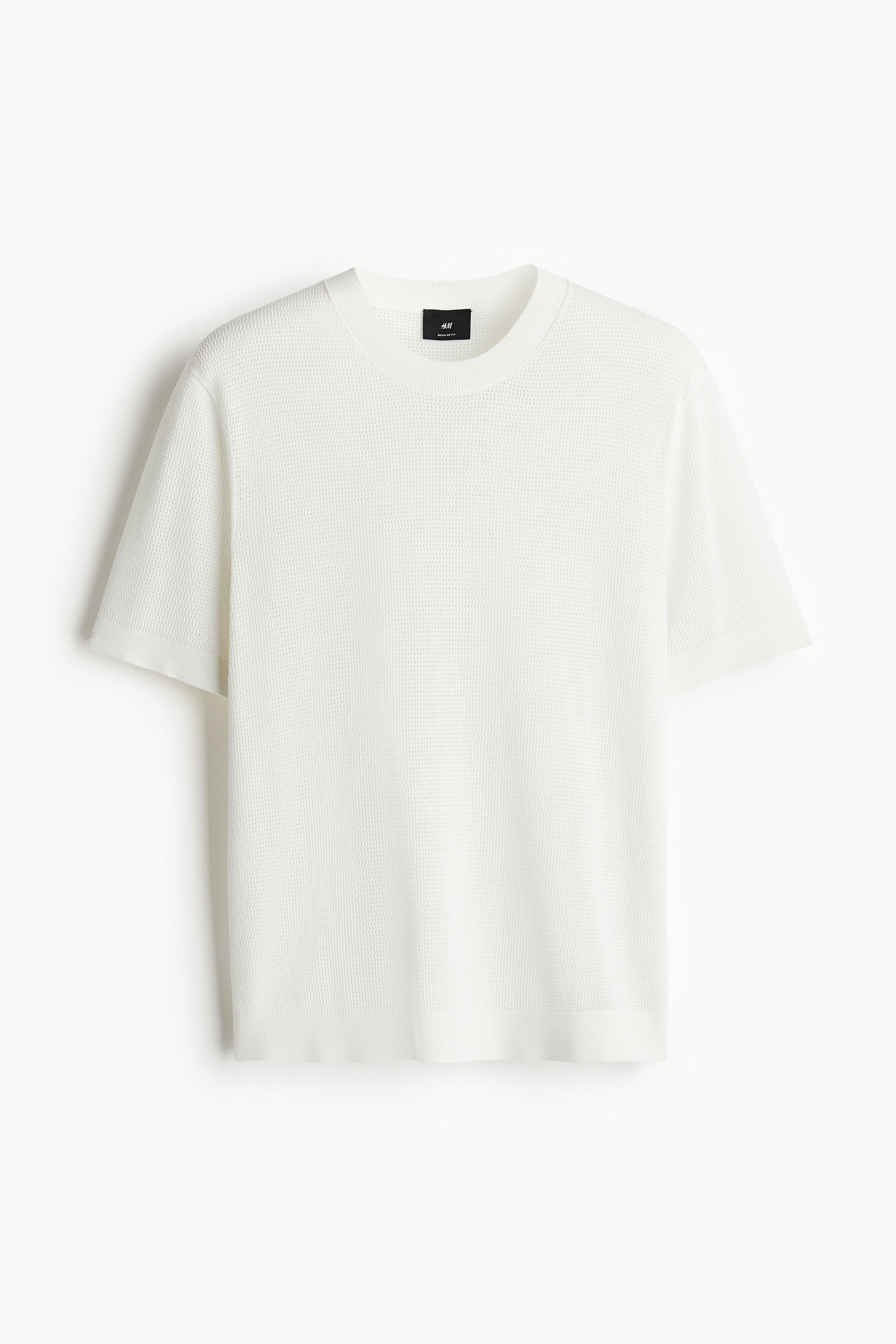 코튼 소재의 홀 니트 티셔츠. 라운드넥. 리브드 마감 옷단. 착용감이 편안하고 클래식한 레귤러핏 실루엣. 이미지