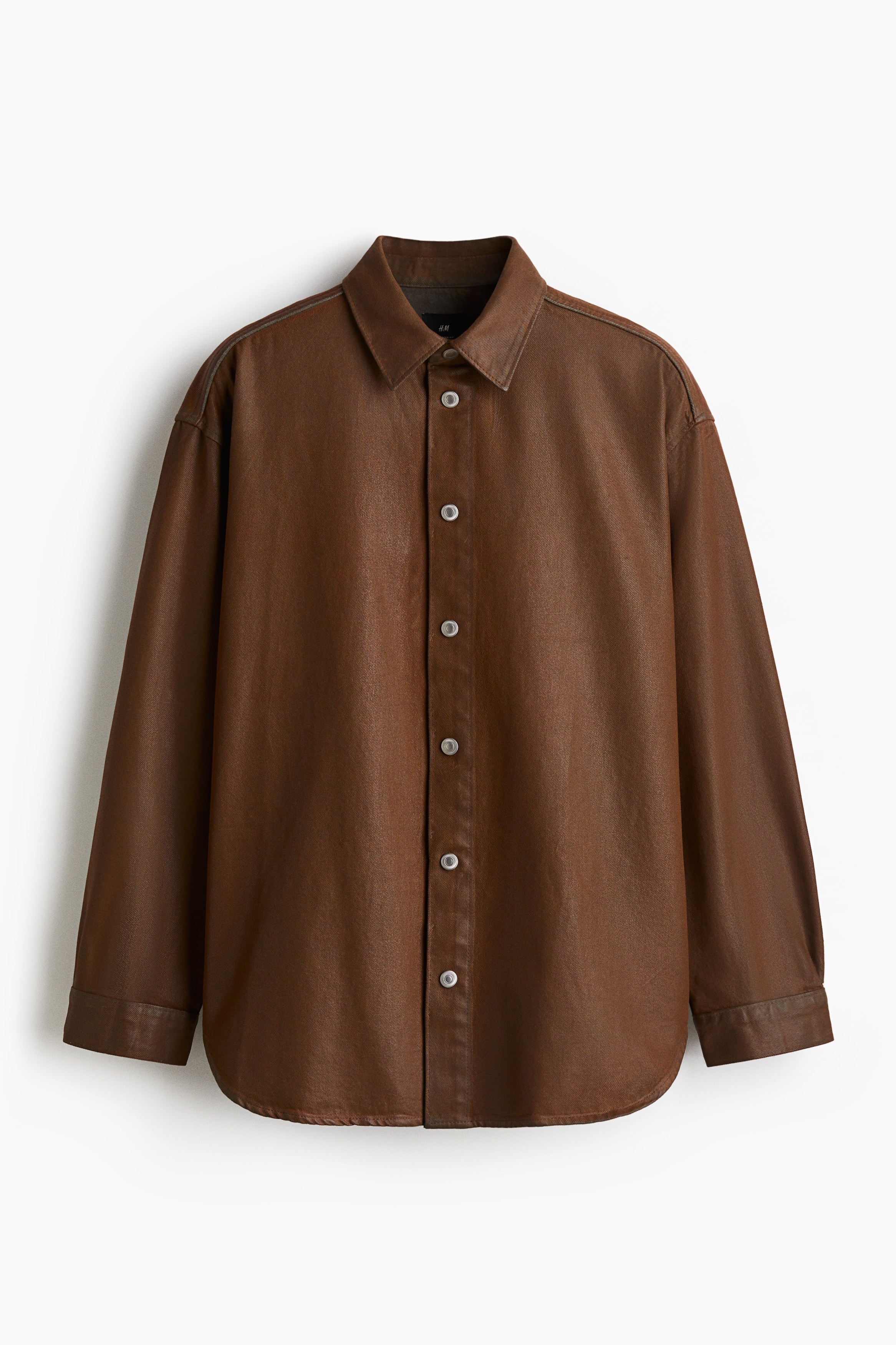 코팅된 톡톡한 코튼 데님 소재의 셔츠. 턴다운 칼라. 금속 버튼으로 여미는 버튼단이 있는 클래식 프런트 스타일. 뒷면 요크. 드롭 숄더. 라운드 헴라인. 긴소매. 플래킷과 버튼이 있는 소맷단. 넉넉하고 매우 루즈한 오버사이즈핏. 이미지