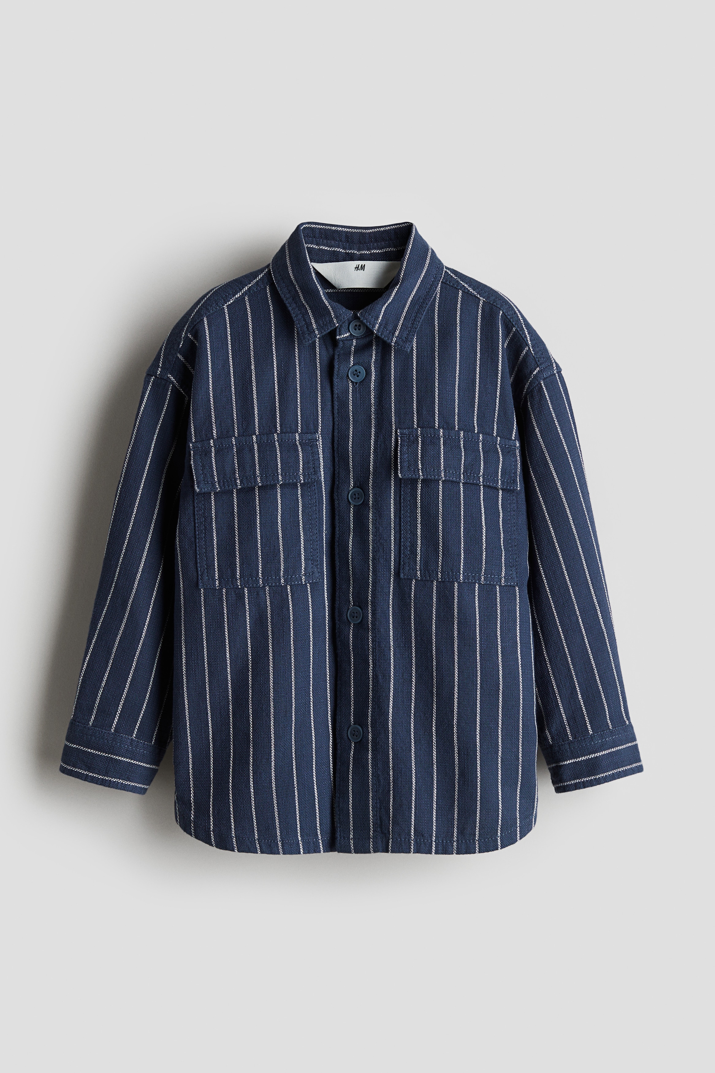 코튼 소재의 루즈핏 셔츠. 가슴 플랩포켓. 턴다운 칼라. 드롭 숄더. 앞면과 소맷단에 버튼이 있음. 라운드 헴라인. 이미지1