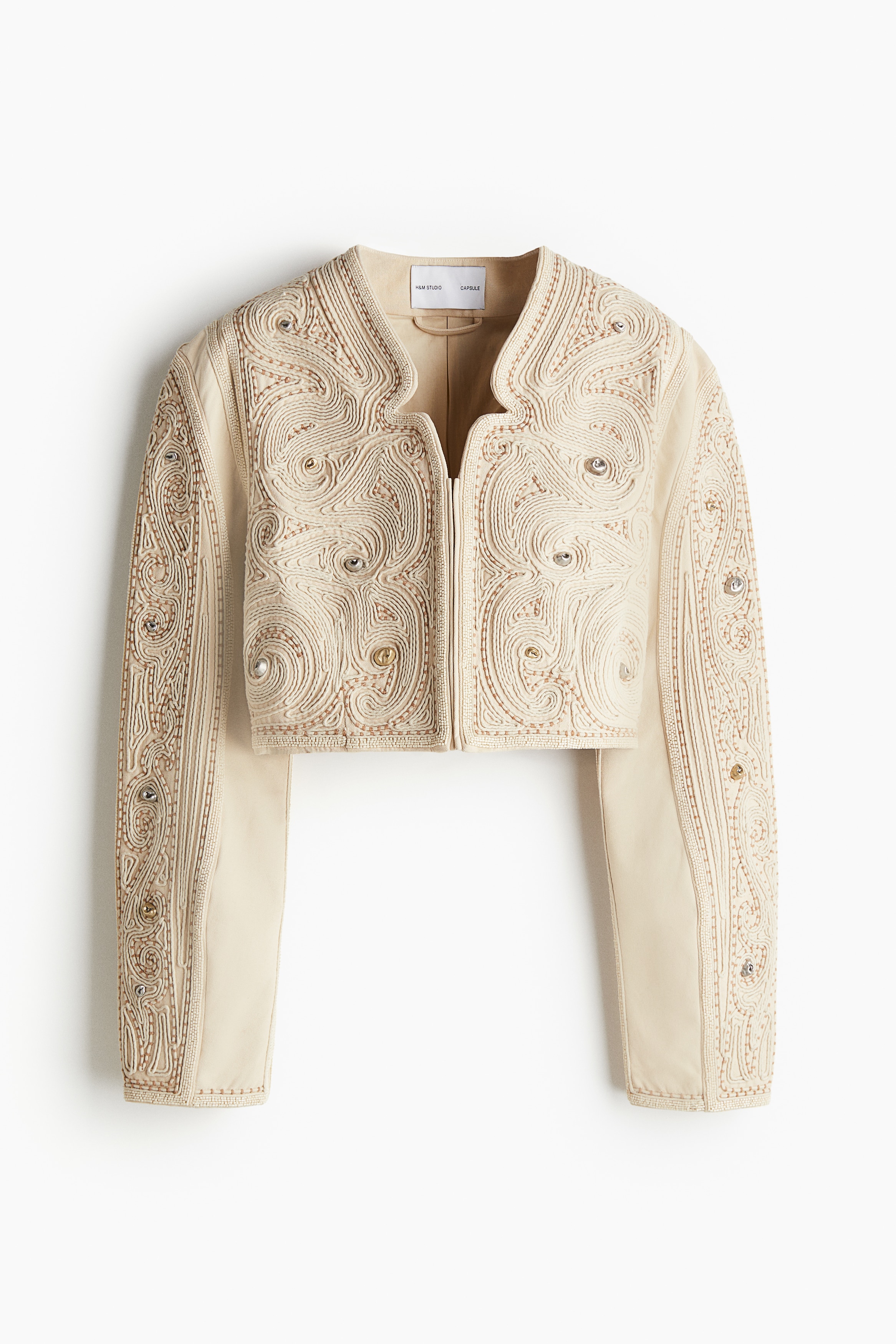 Studio Collection. 톡톡한 코튼 캔버스 소재의 짧은 재킷. 섬세한 자수로 마감됨. 불규칙적인 금속 스터드와 유리 비즈 장식. 앞면 컷아웃 디테일 장식적인 느낌을 더하는 V넥. 히든 후크로 여밈. 내부 웰트포켓. 긴소매. 소매 부분 거싯이 활동성을 높인 제품. 코튼 보일 안감. 이미지