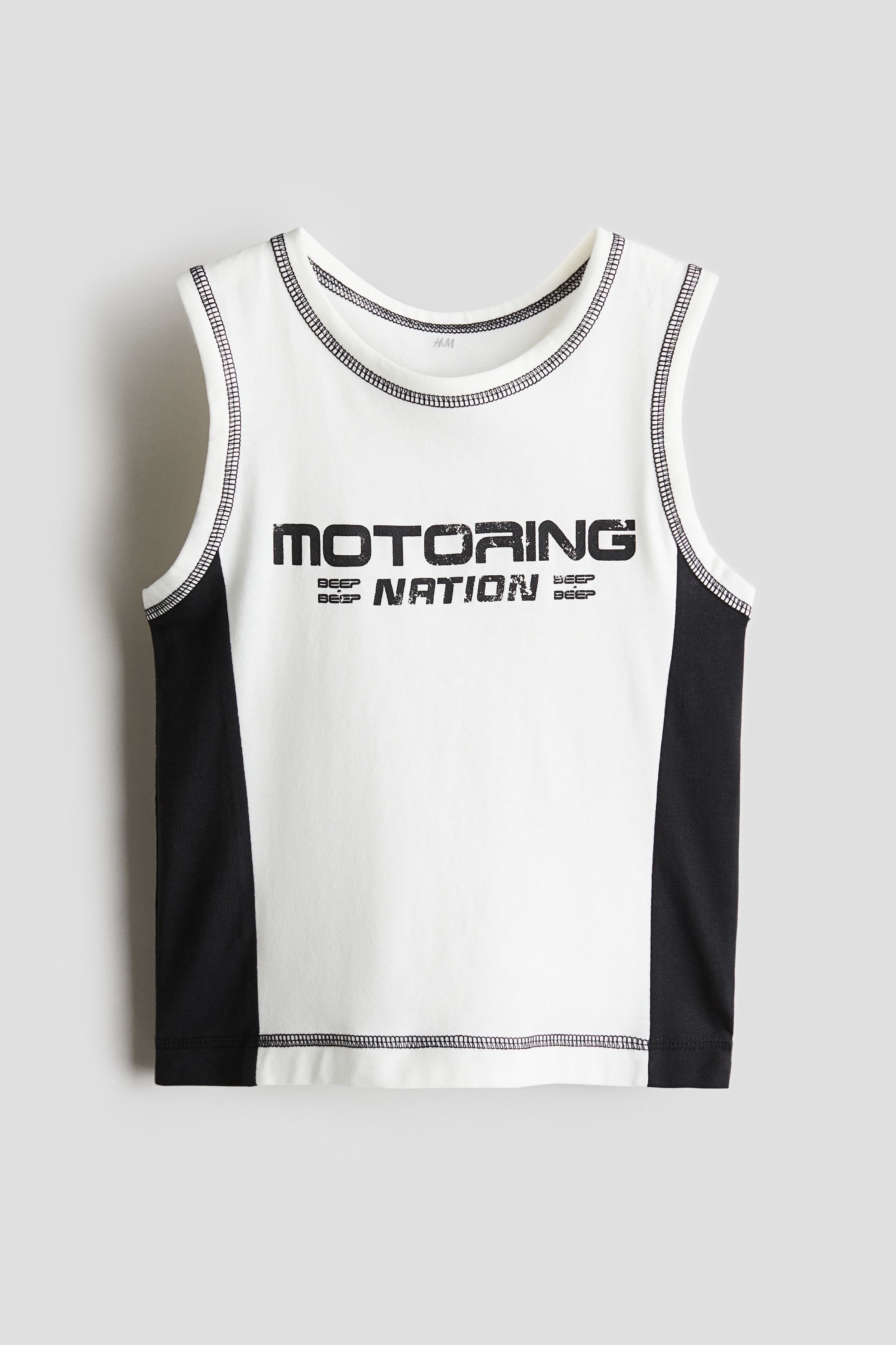 부드러운 코튼 저지 소재의 슬리브리스 탑. 앞면 레터링 프린트 디테일. 오버로크 솔기 장식. 이미지