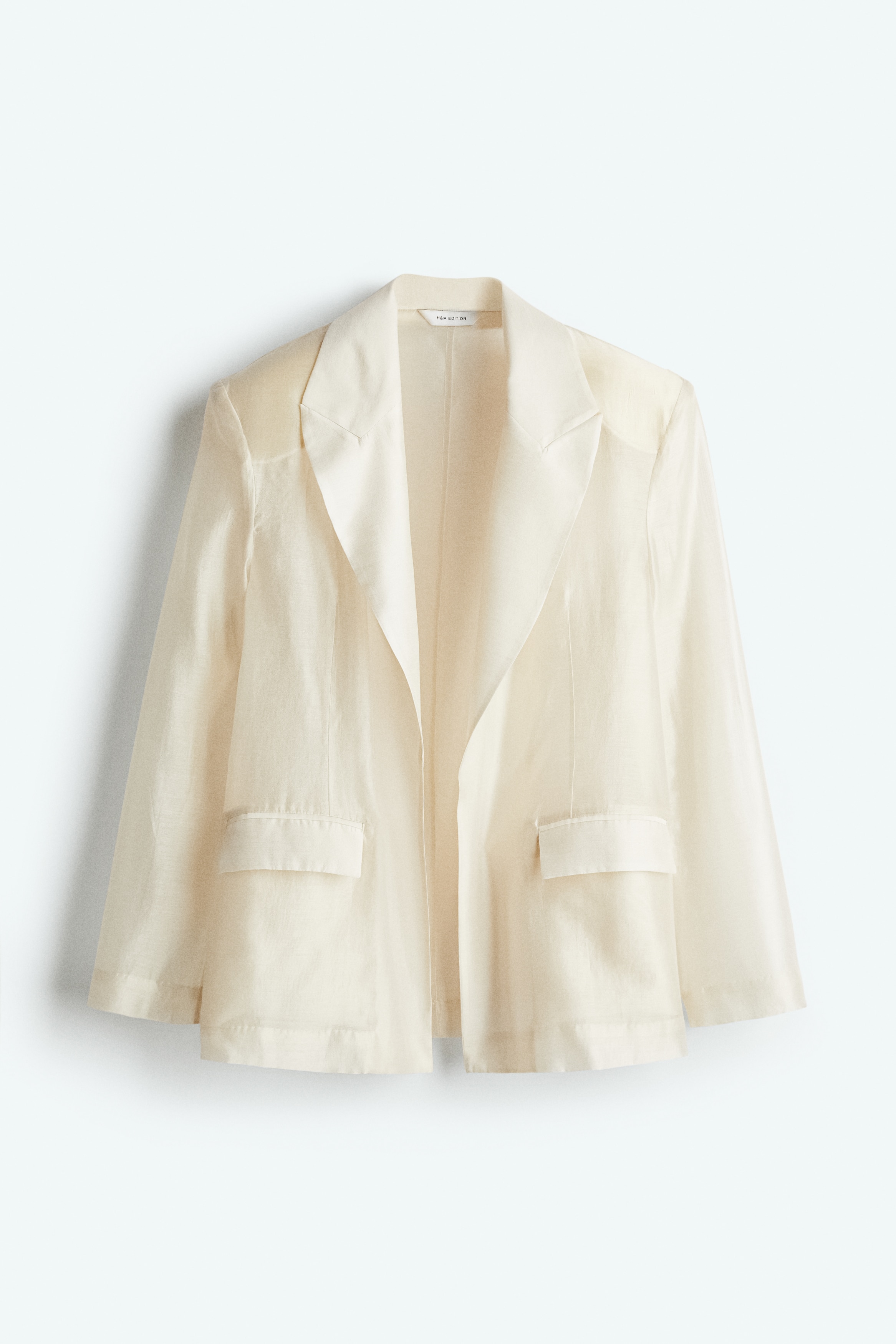 얇은 광택성 소재의 오버사이즈 재킷. 피크트 라펠. 클로저 생략. 플랩이 있는 앞면 웰트포켓. 숄더 패드로 어깨 라인을 강조한 디자인. 안감 생략. 이미지