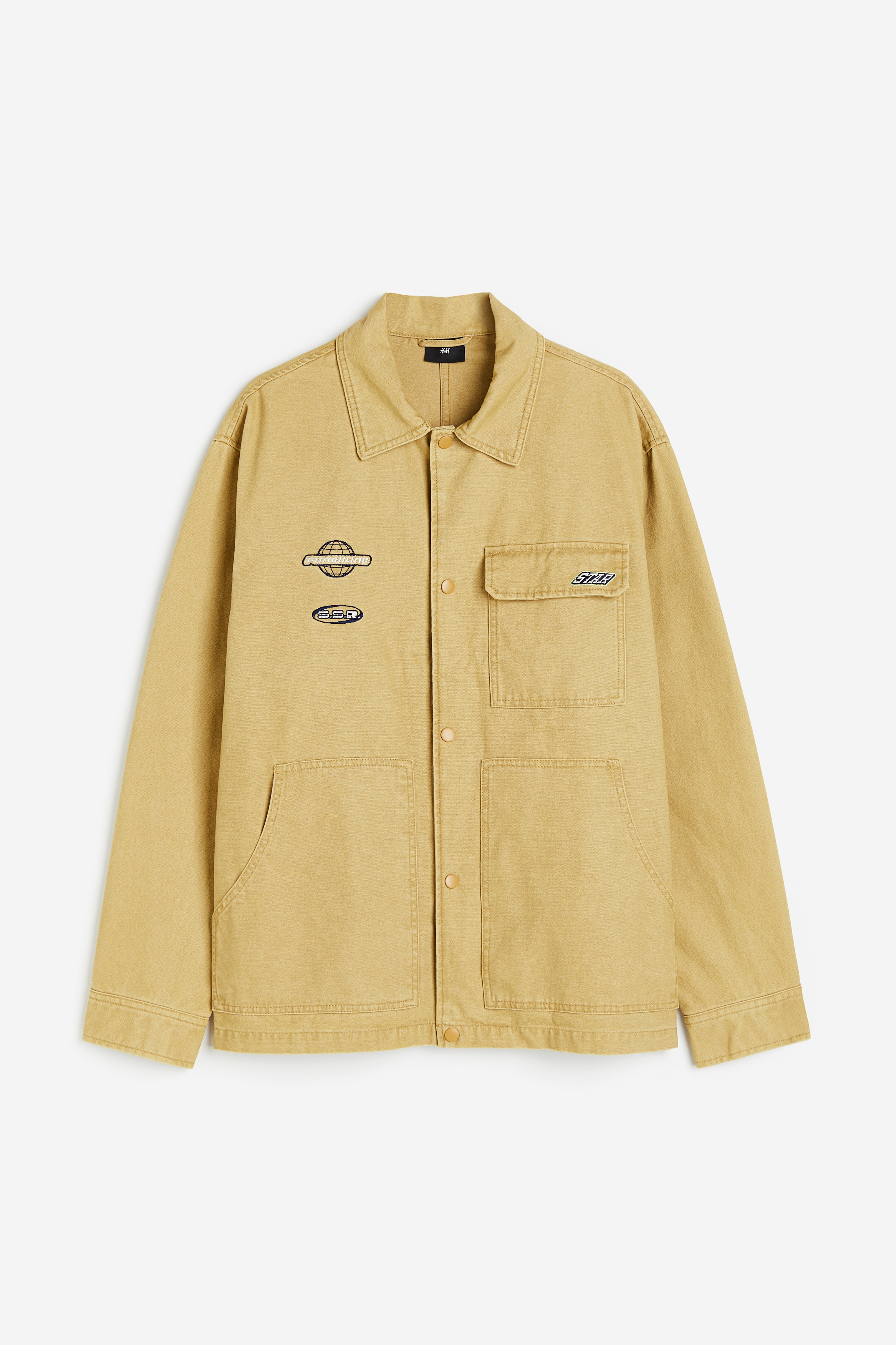 가슴 부분에 자수 장식이 있는 코튼 트윌 소재의 재킷. 루즈핏. 칼라와 앞면 스냅버튼이 있음. 긴소매. 소맷단 버튼. 가슴 플랩포켓. 앞면 하단 포켓. 안감 생략. 이미지