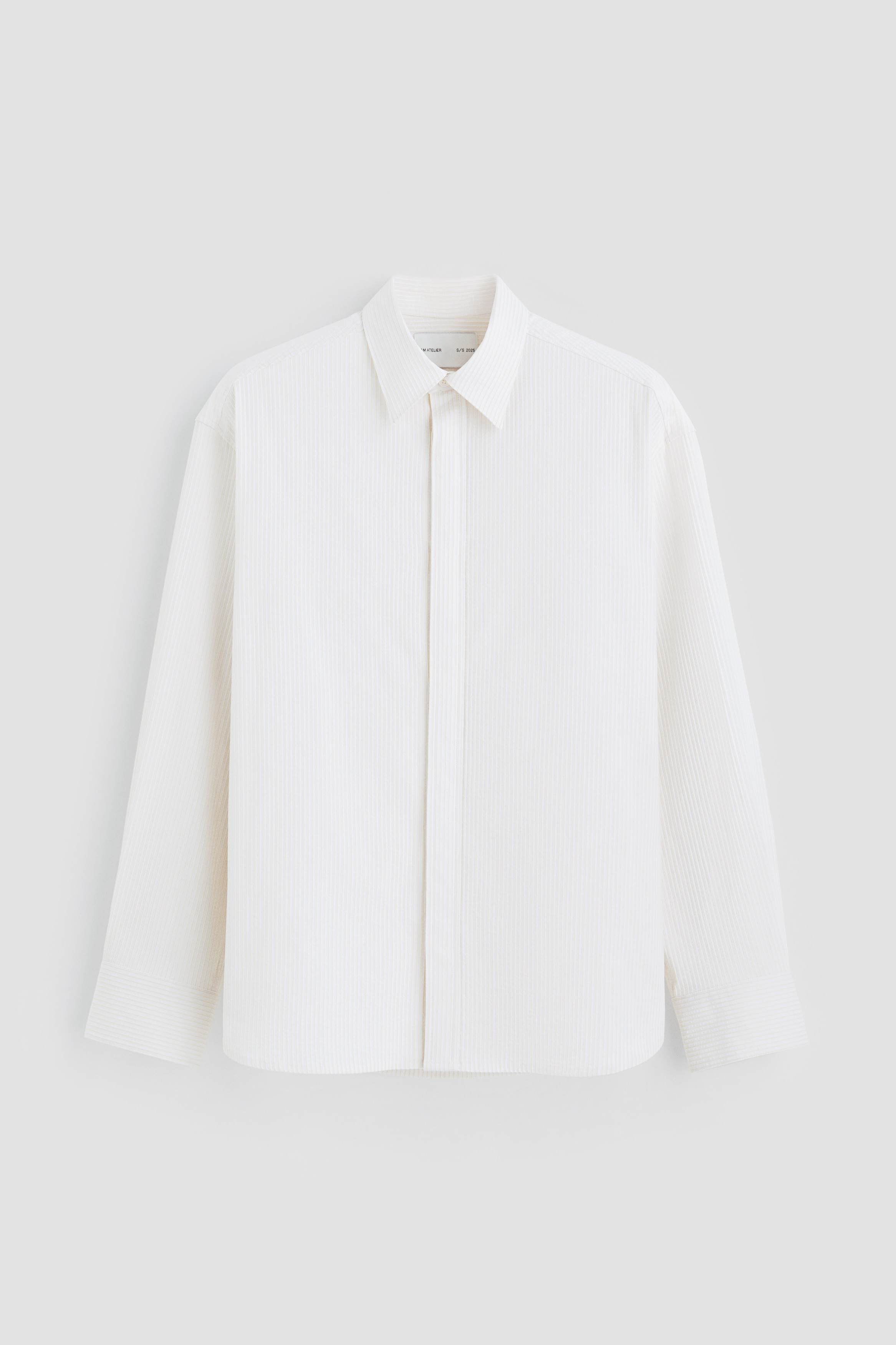 H & M Atelier. 이탈리아 원단 제조업체인 Pontetorto에서 공급하는 코튼과 비스코스가 혼방된 자카드 셔츠. 턴다운 칼라. 앞면 히든 버튼 플래킷. 박스 플리츠가 잡힌 뒷면 요크 디테일. 오버사이즈핏. 긴소매. 플래킷과 버튼이 있는 소맷단. 라운드 헴라인. 이미지