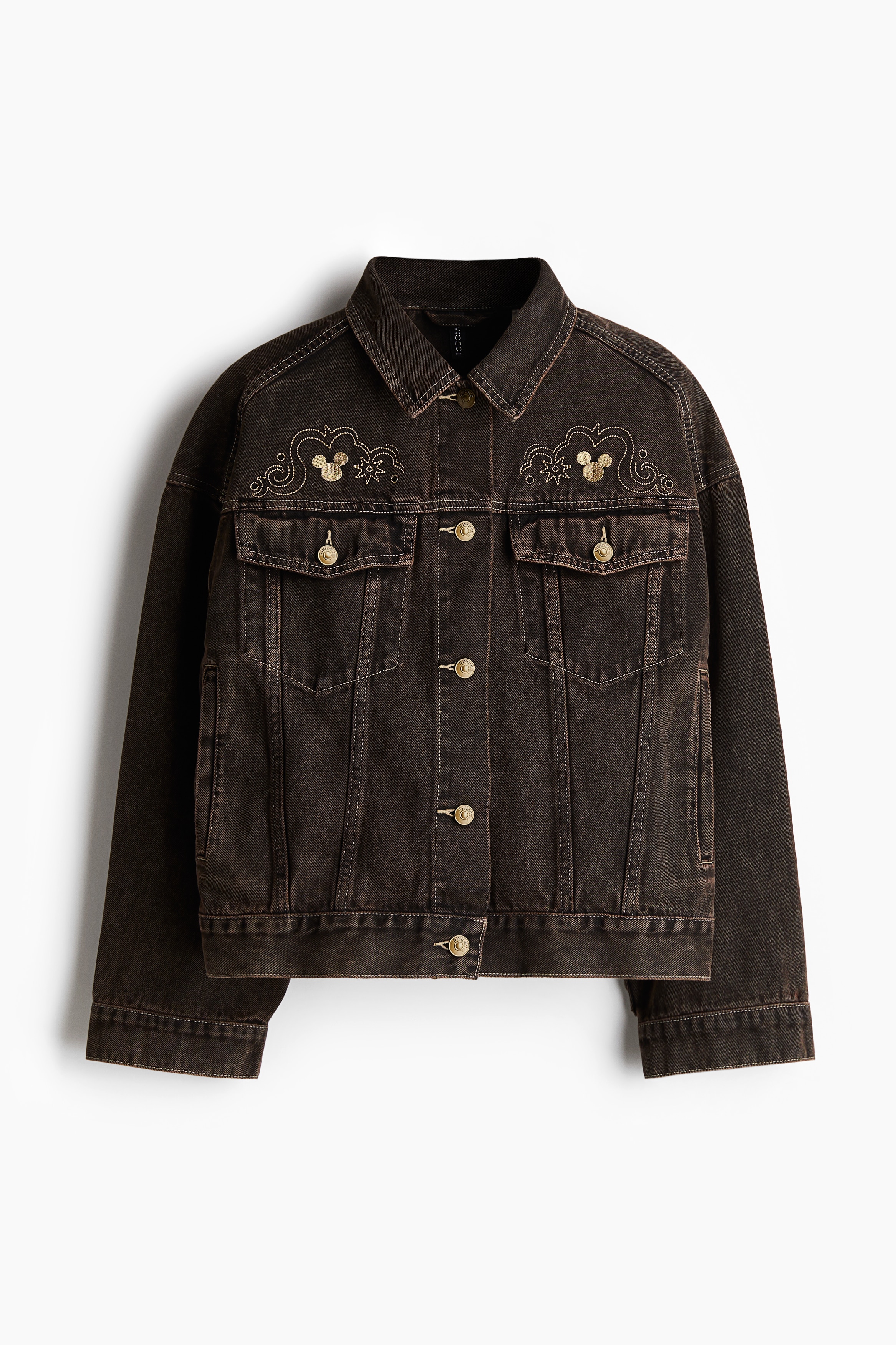 장식 디테일이 있는 탄탄한 코튼 데님 소재의 트러커 스타일 재킷. 칼라와 앞면 금속 버튼이 있음. 어깨 앞면 솔기. 앞뒷면 요크. 루즈핏. 드롭 숄더. 소맷단 버튼. 버튼이 있는 가슴 플랩포켓. 옆면 웰트포켓. 양쪽 옆면 하단의 탭과 버튼으로 핏 조절. 이미지