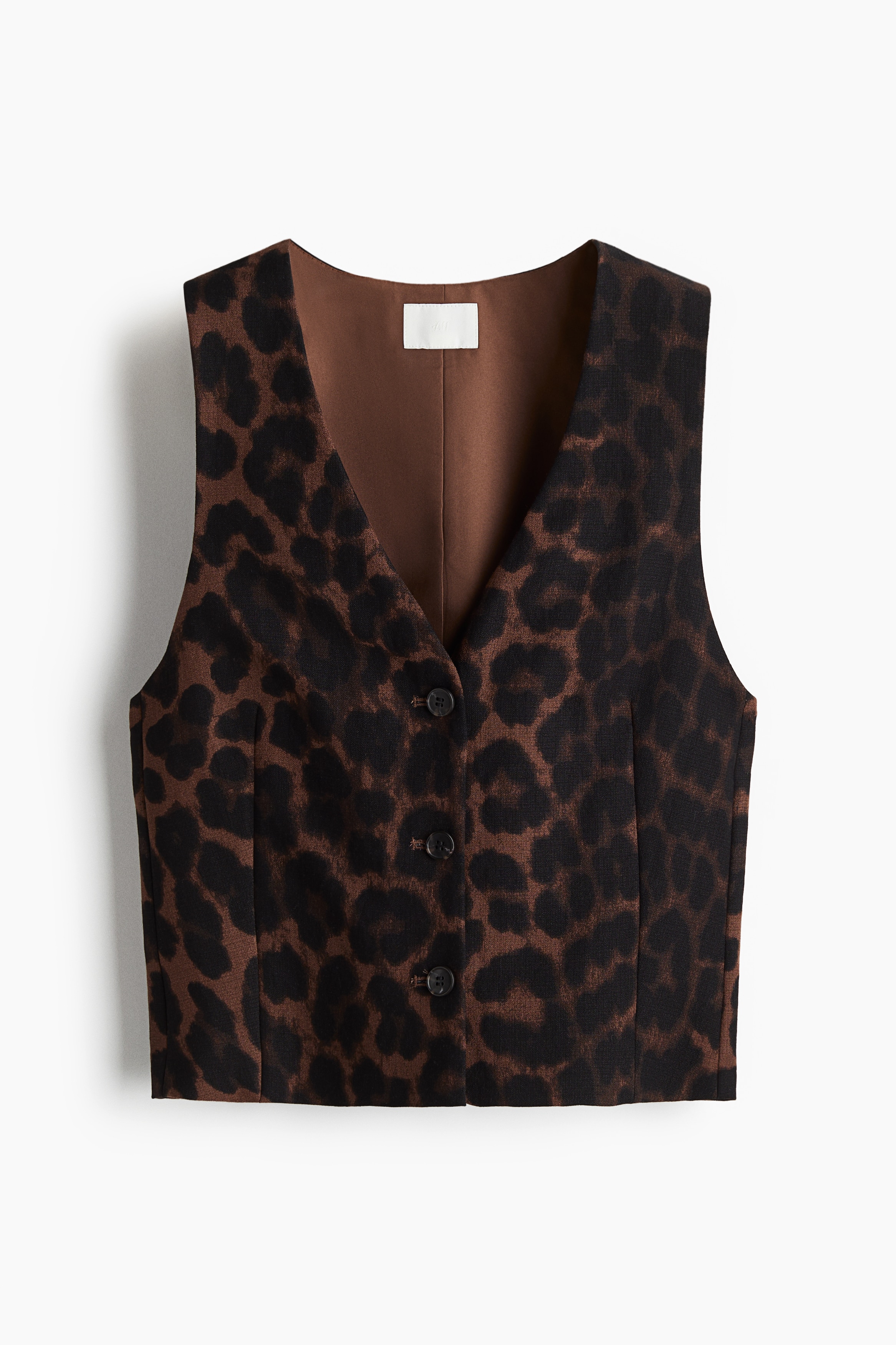 짧고 피트되는 스타일의 베스트. 깊게 파인 V넥. 앞면 버튼 클로저. 앞면에 입체감을 주는 다트가 잡혀 있어 바디 라인이 드러나는 실루엣. 안감 부착. 이미지