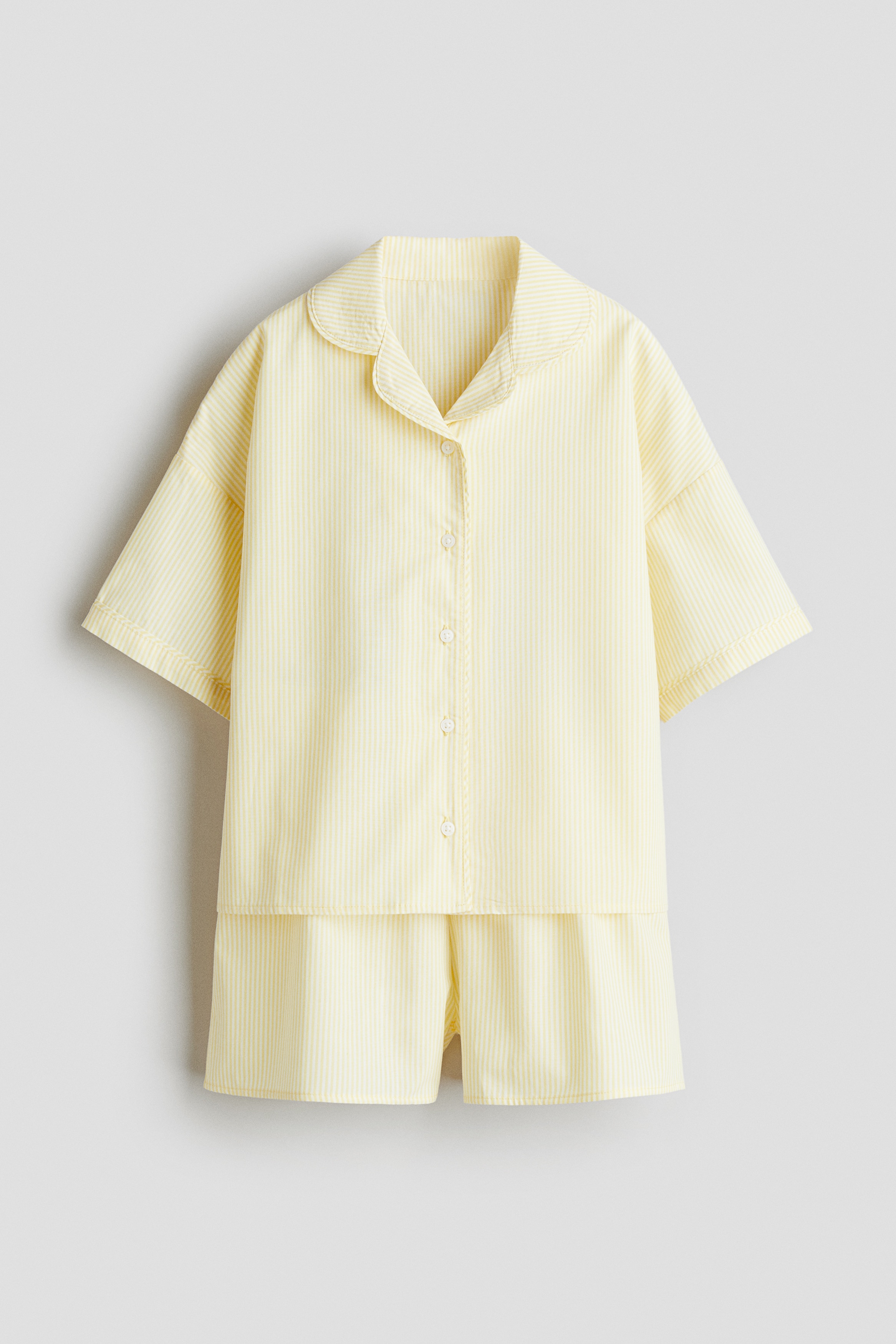 빳빳한 코튼 포플린 소재의 파자마 상하 세트. 상의 - 버튼업 스타일의 반소매 셔츠. 캠프 칼라. 드롭 숄더. 하의 - 신축성 허릿단의 반바지. 이미지