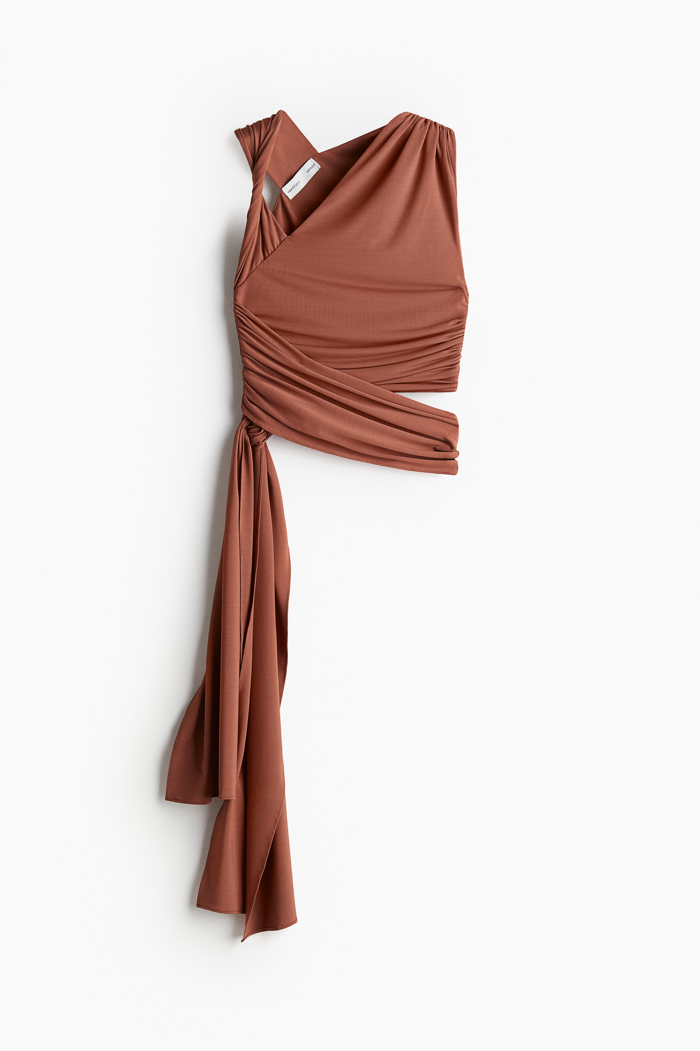 Studio Collection. 부드러운 스트레치 저지 소재의 피트되는 크롭트 탑. 슬리브리스. 언발란스 네크라인. 한쪽 어깨에 꼬임 스트랩이 있으며, 반대쪽 어깨에 주름이 잡힌 스타일. 옆면 솔기에도 주름이 잡혀 있으며, 물 흐르듯 떨어지는 와이드한 끈을 허리 위에 감아 한쪽 옆면에서 매듭짓는 디자인. 안감 부착. 이미지