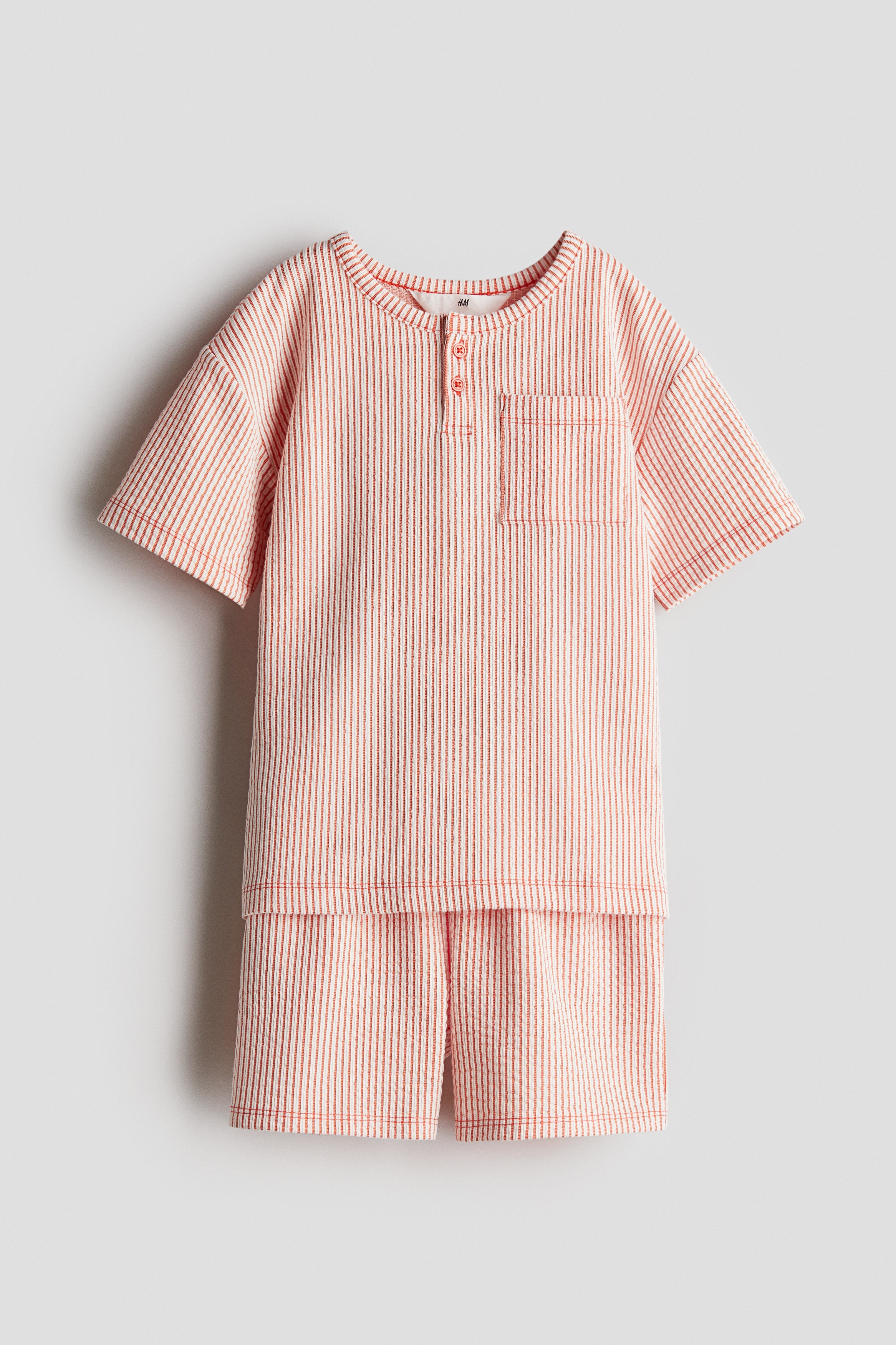 시어서커 느낌의 부드러운 저지 상하의 세트. 상의 - 반소매 헨리탑. 라운드넥. 버튼 플래킷. 앞면 버튼 2개. 가슴 포켓. 드롭 숄더. 하의 - 드로스트링이 있는 신축성 허릿단의 반바지. 뒷면 포켓. 이미지