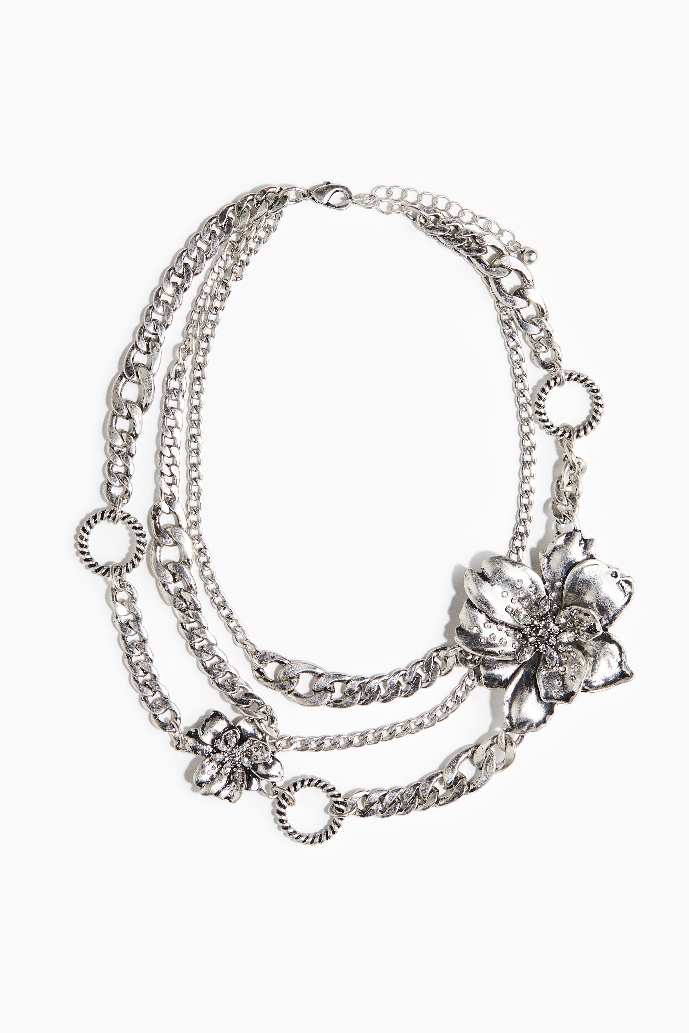 각각 다른 디자인과 길이의 체인 여러 줄을 사용하여 레이어드 효과를 준 목걸이. 링 디테일과 플라워 펜던트로 장식됨. 트리거 후크로 길이 조절 가능. 이미지