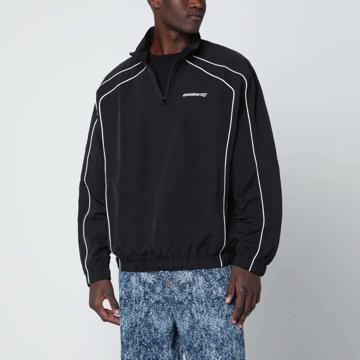 어웨이크 뉴욕 스포츠 재킷은 블랙 색상에 하프 집업 하이 칼라, 긴 소매, 엘라스틱 커프스와 밑단, 그리고 가슴 부분에 대조적인 로고 자수가 특징입니다. 이미지