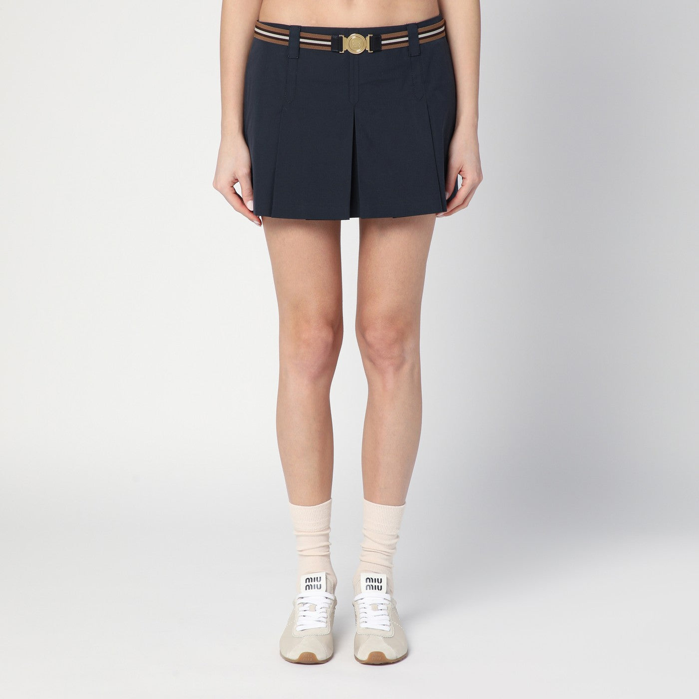 미우미우의 블루 코튼 블렌드 미니스커트는 골드 마감의 로고 메탈 버클이 달린 리본 허리 벨트, 옆면 후크 및 지퍼 잠금, 전면 플리츠, 뒷면 로고 자수가 특징입니다. 이미지