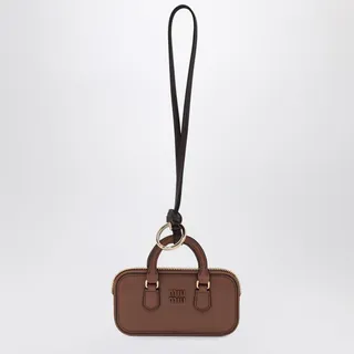 미우미우의 코냑색 레더 아르카디 백 모양 트리크는 스트랩이 달린 링, 뒷면 거울, 그리고 전면의 페인티드 메탈 로고 레터링이 특징입니다. 이미지
