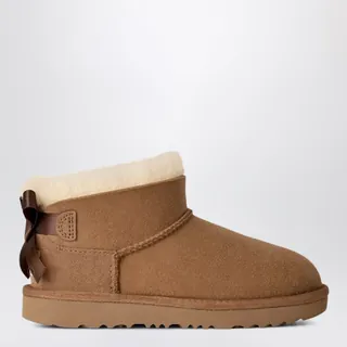 UGG 울트라 미니 베일리 보우 양털 부츠입니다. 체스트넛 컬러의 스웨이드 어퍼와 뒷면의 장식용 새틴 리본이 특징입니다. 오버록 스티치 디테일과 따뜻한 UGGplush™ 안감 및 인솔, 가벼운 사탕수수 EVA 아웃솔을 적용하여 편안한 착화감을 제공합니다. 뒷면에는 UGG® 로고 라벨이 부착되어 있습니다. 이미지
